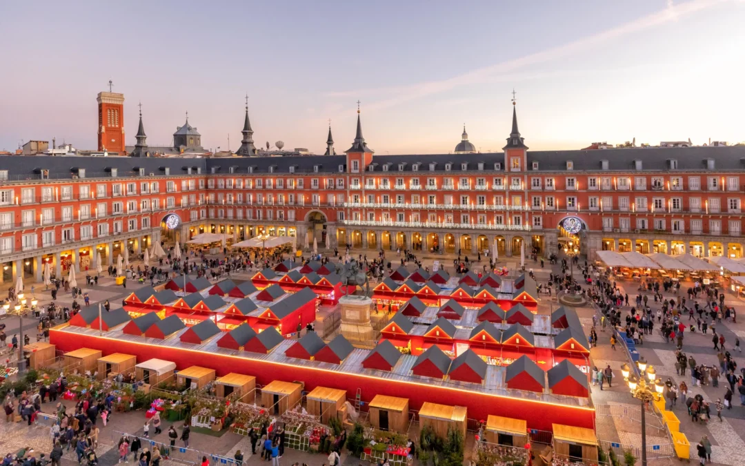 Mercadillo navideño en la Plaza Mayor de Madrid con casetas rojas, luces y ambiente festivo.