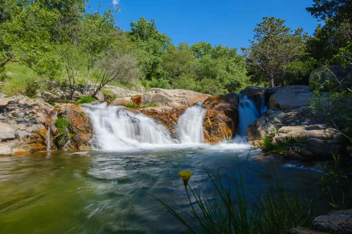 Cascada y poza natural en la Charca Verde de La Pedriza, rodeada de rocas y vegetación.