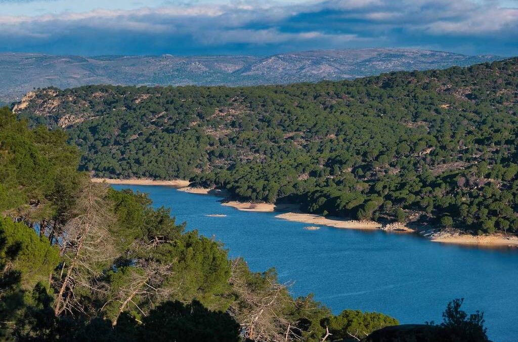 Embalse rodeado de bosque y montañas, agua azul y paisaje natural típico de las playas fluviales cerca de Madrid